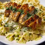 Steaming pasta dish with sliced chicken and green herbs.