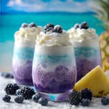 Two glasses of blue and white drinks with blueberries on the side.