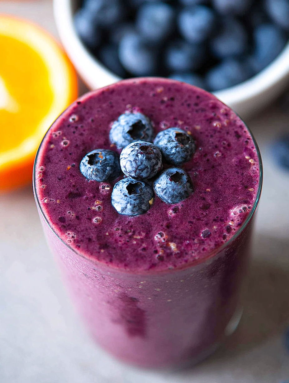 A glass of blueberry smoothie with blueberries on top.
