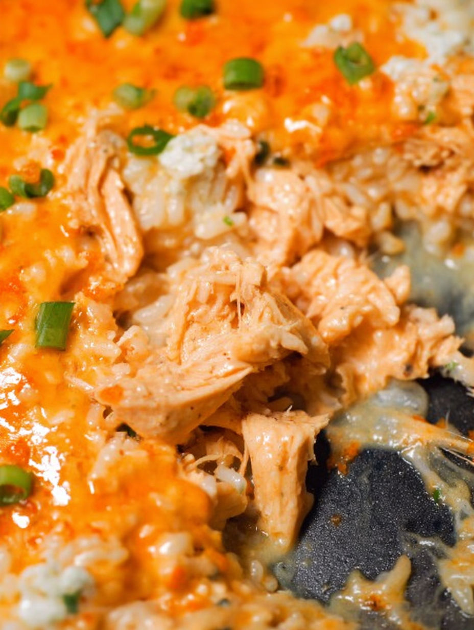 A close up of a piece of chicken in a cheesy buffalo chicken rice casserole.