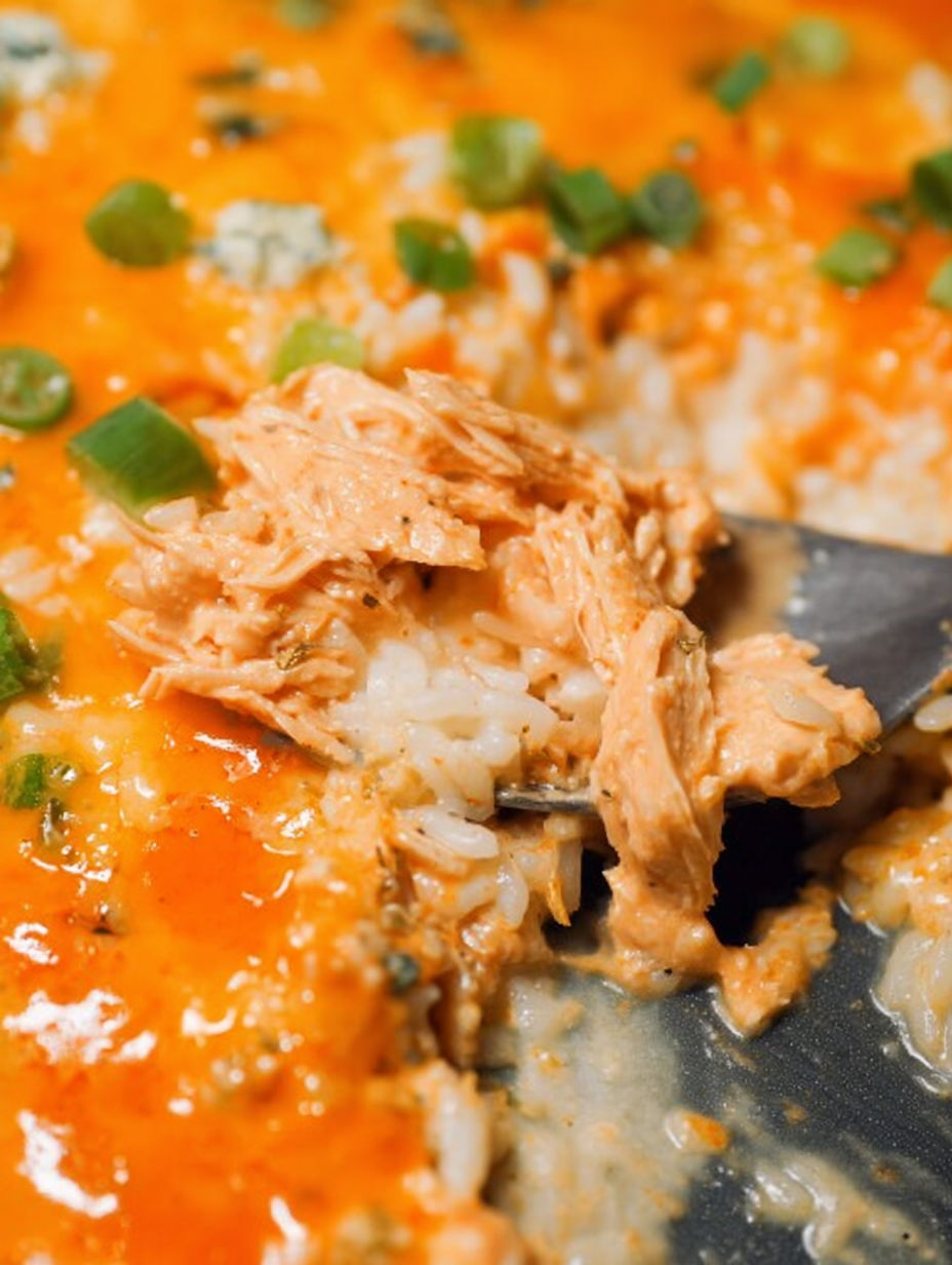 A spoon is in a cheesy buffalo chicken rice casserole.