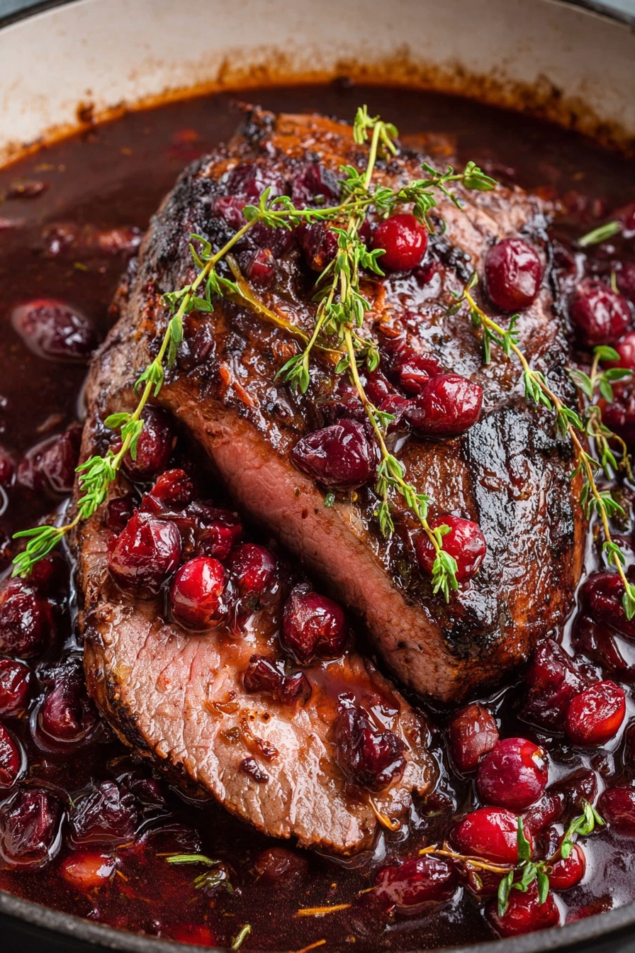 A piece of roast beef with cranberries and a sprig of rosemary.