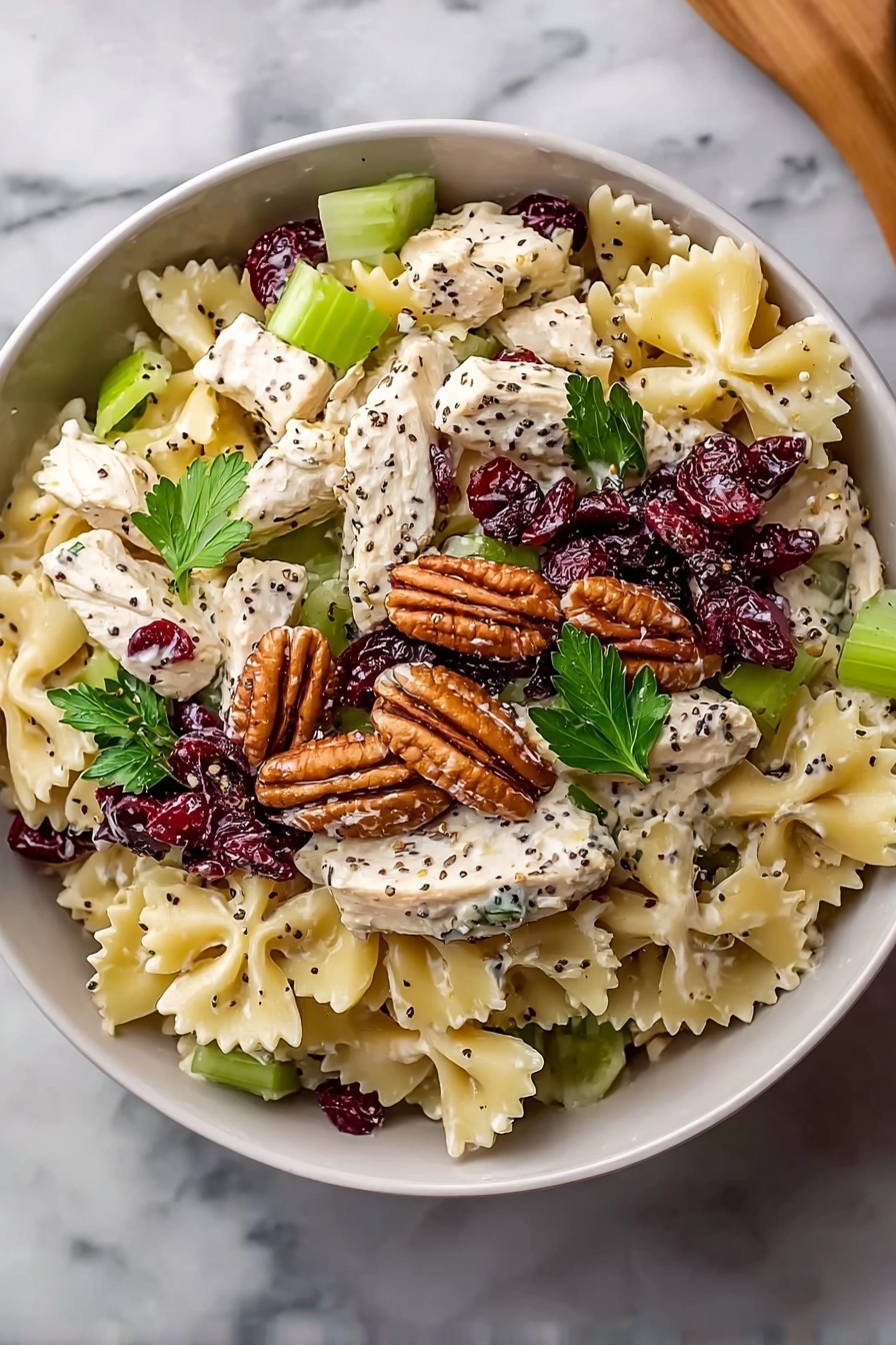 A bowl of pasta salad with chicken, cranberries, and pine nuts.