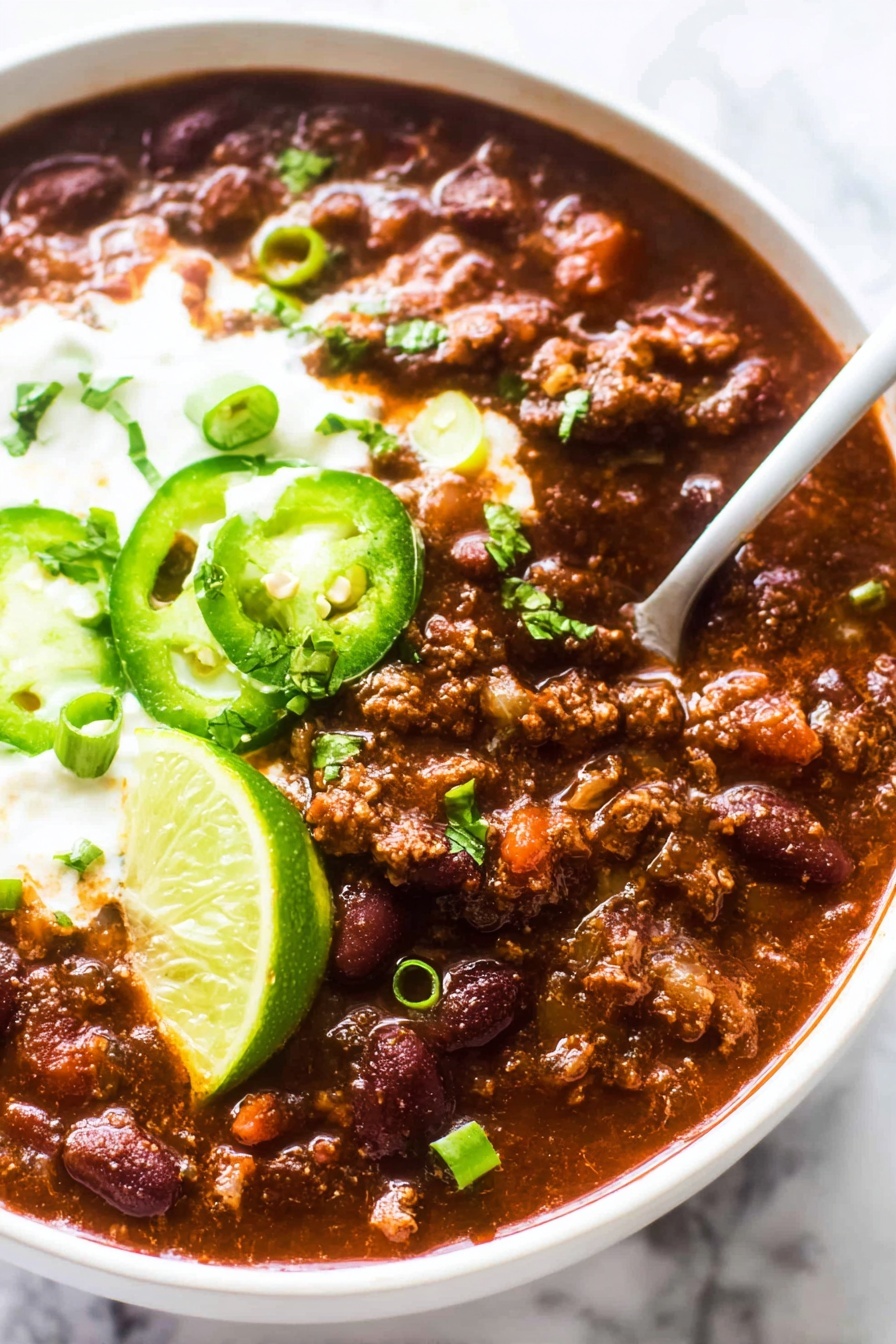 A bowl of chili with green onions and lime wedges.