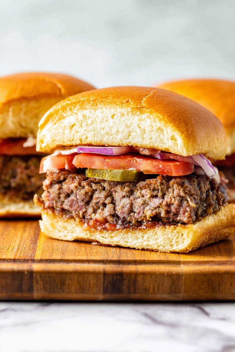Two bison burgers with tomatoes and pickles.