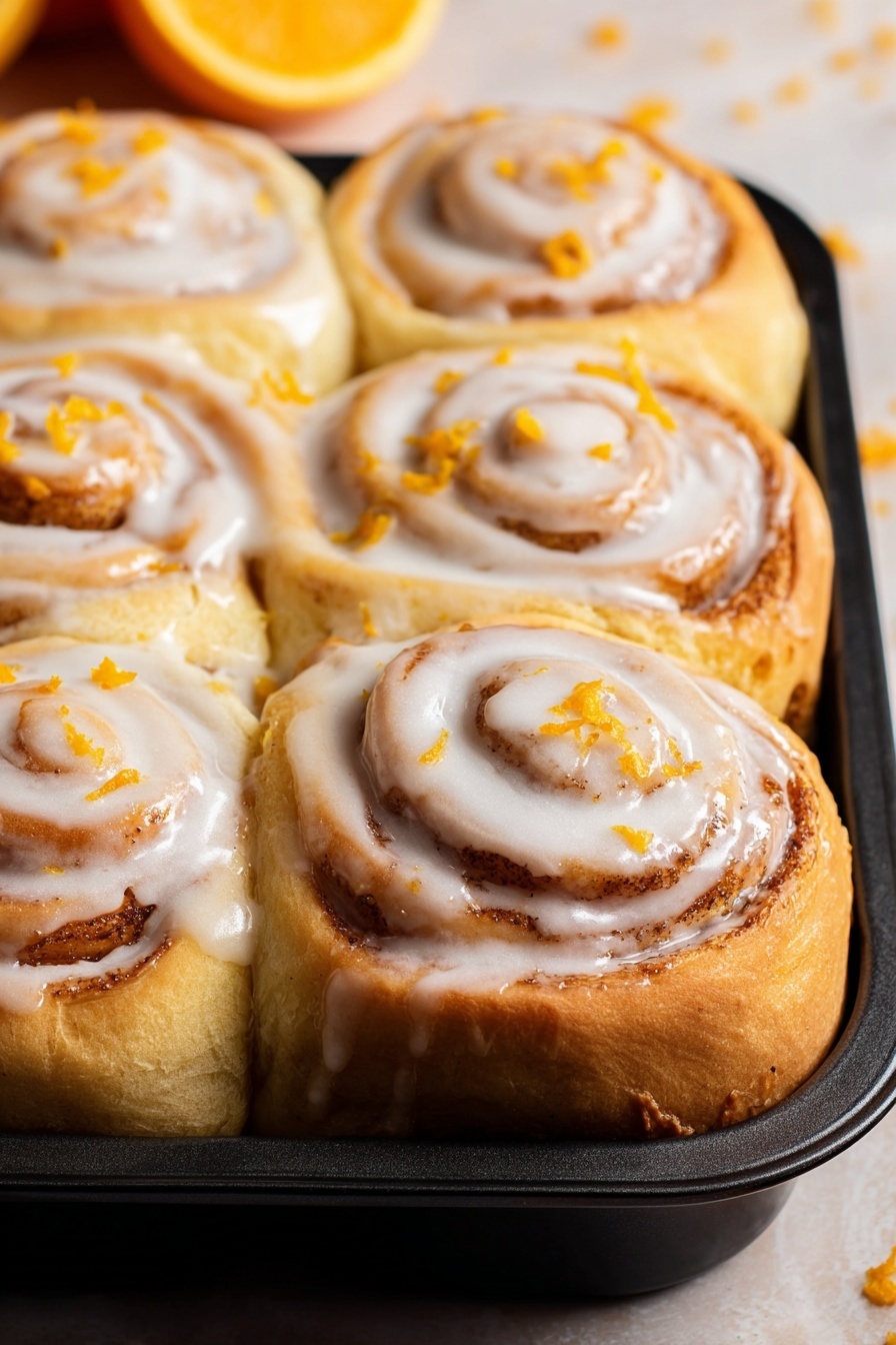 A tray of orange rolls with white icing.