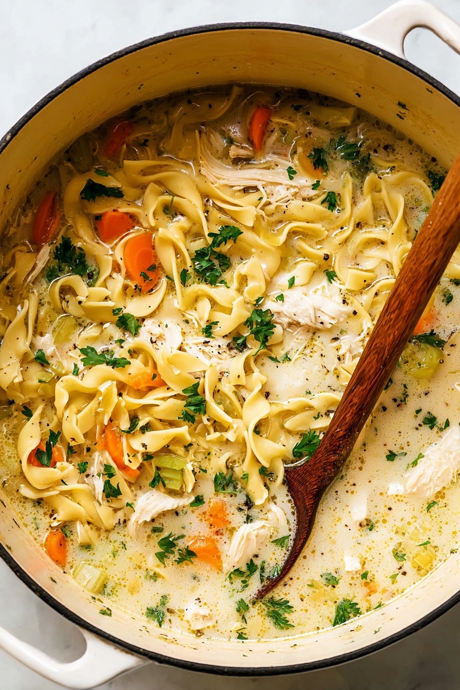 A wooden spoon in a bowl of creamy chicken noodle soup.