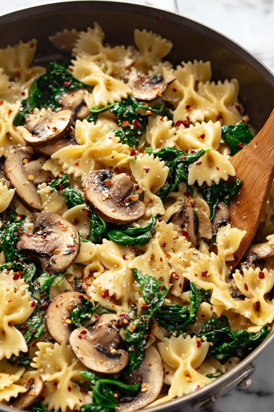A bowl of pasta with mushrooms and spinach.