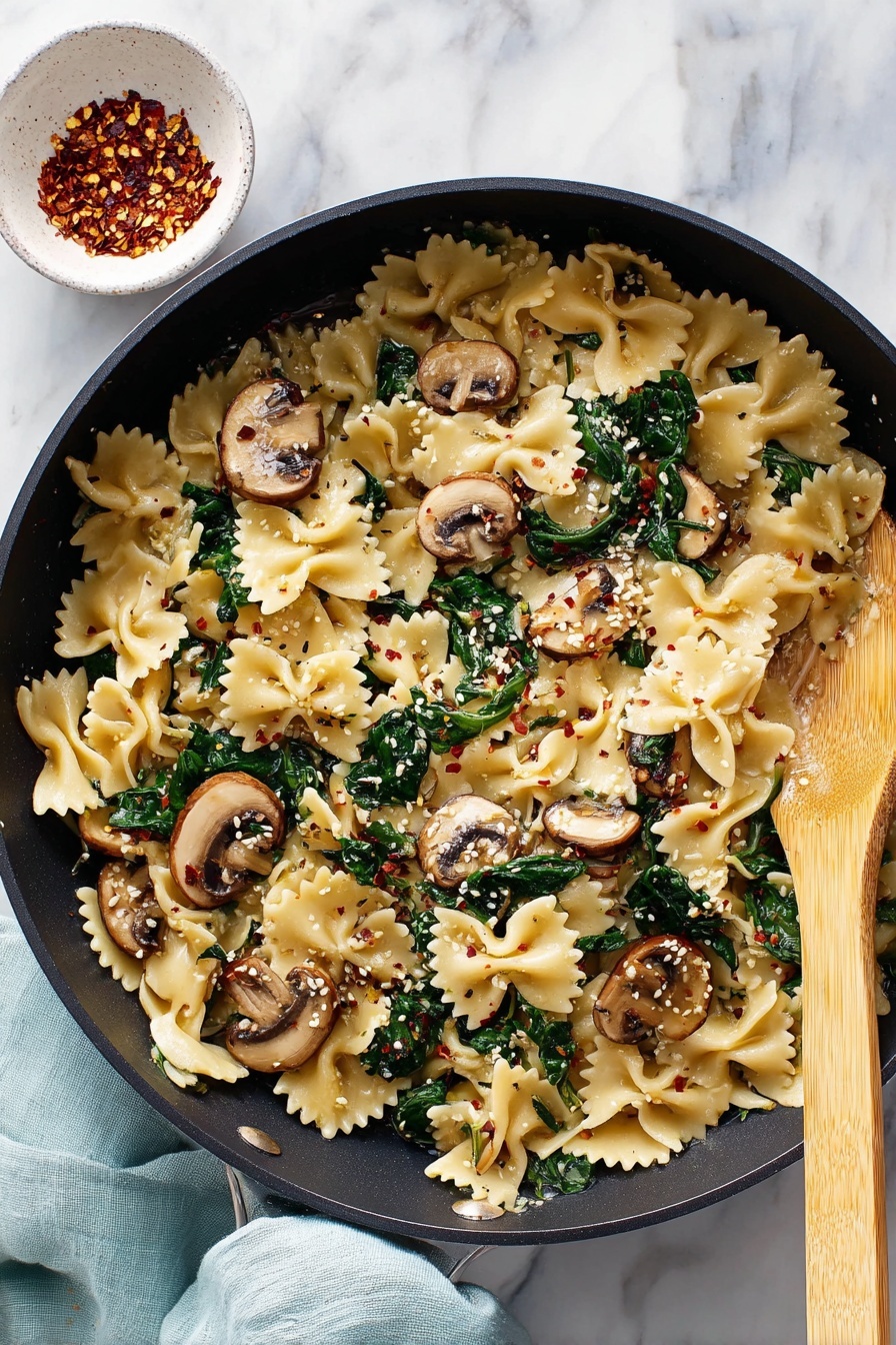 A bowl of pasta with mushrooms and spinach.