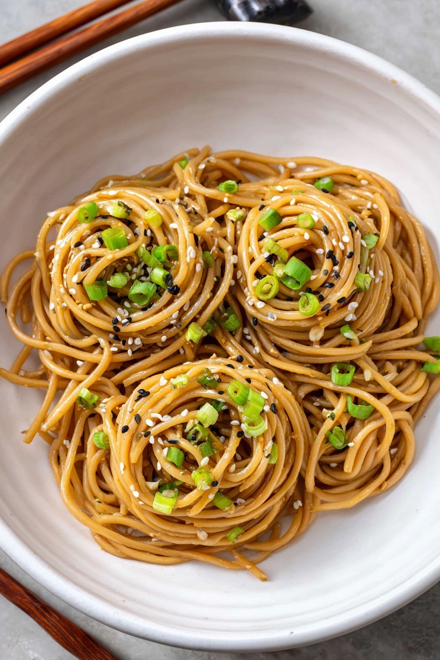 A bowl of sesame noodles with green onions.