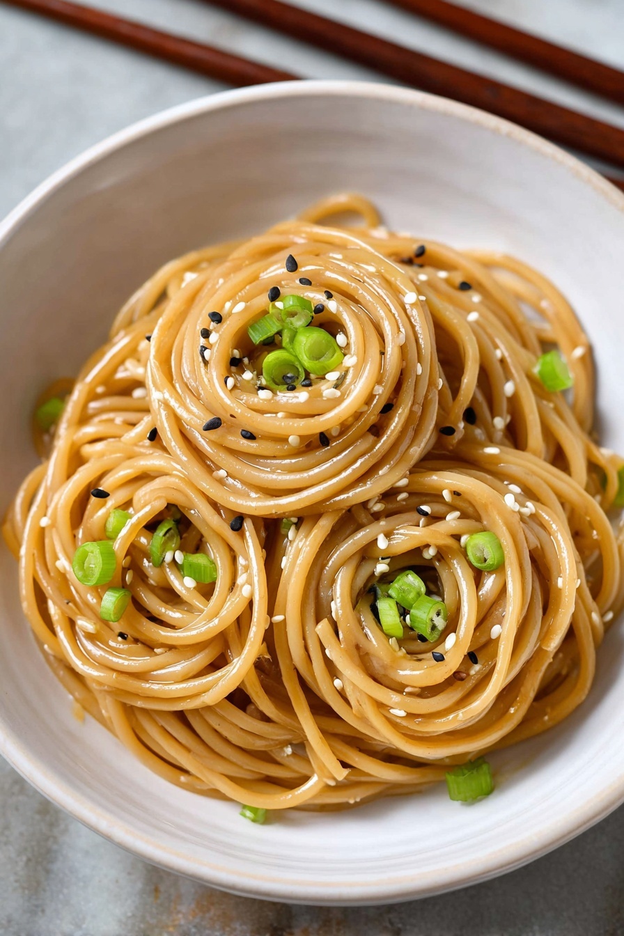 A bowl of sesame noodles with green onions.