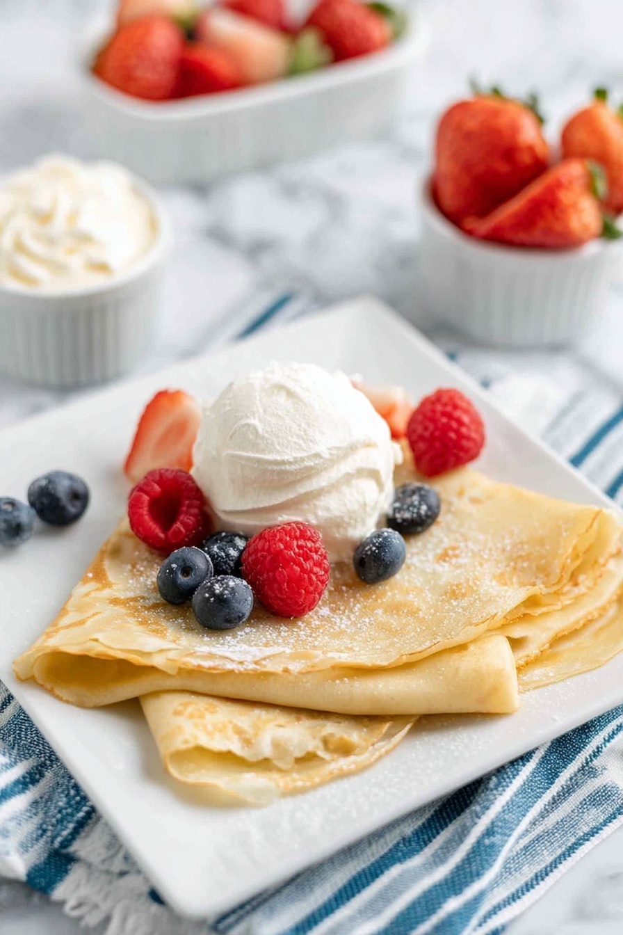 A plate of crepes with strawberries and whipped cream.