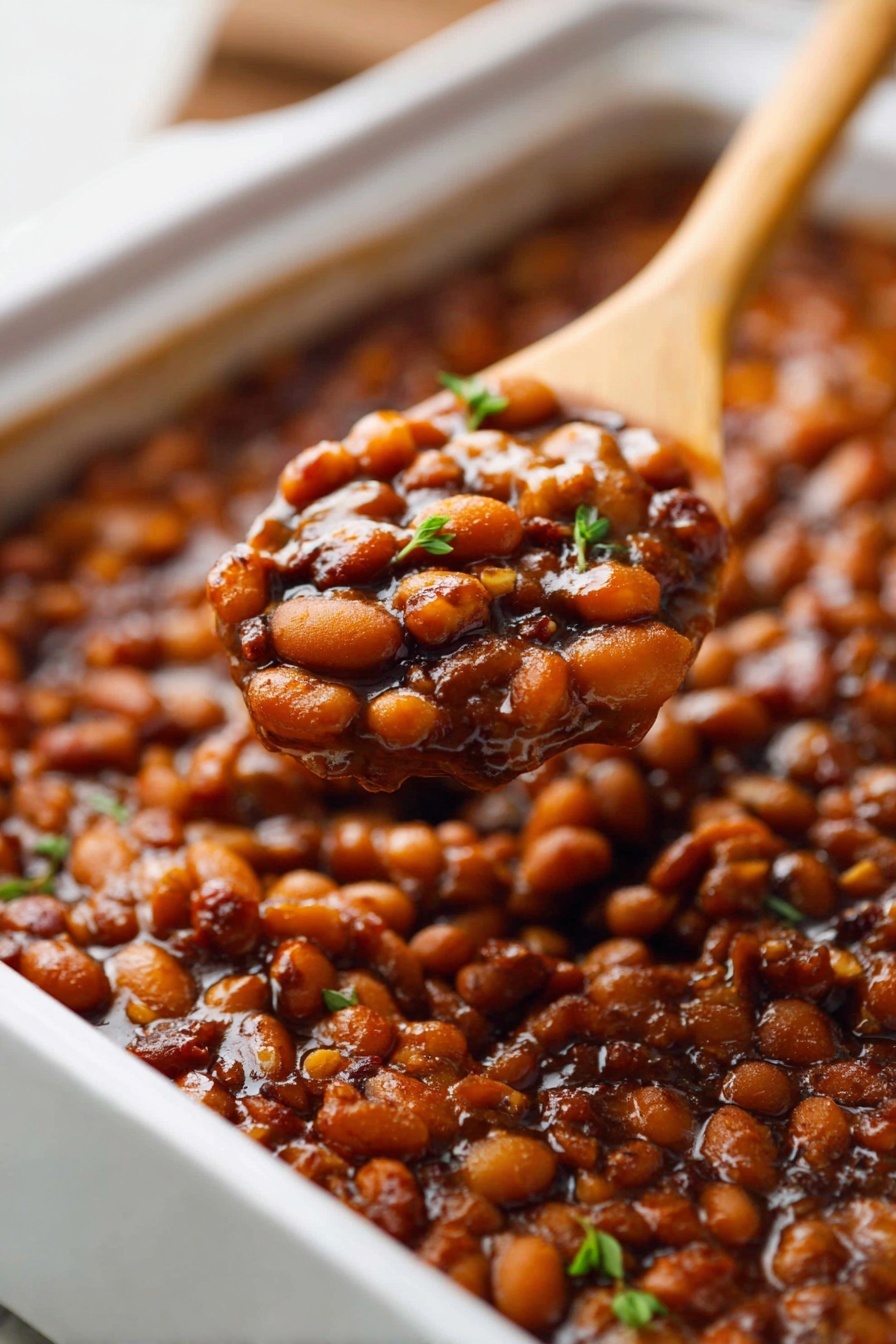 A wooden spoon is scooping up baked beans.