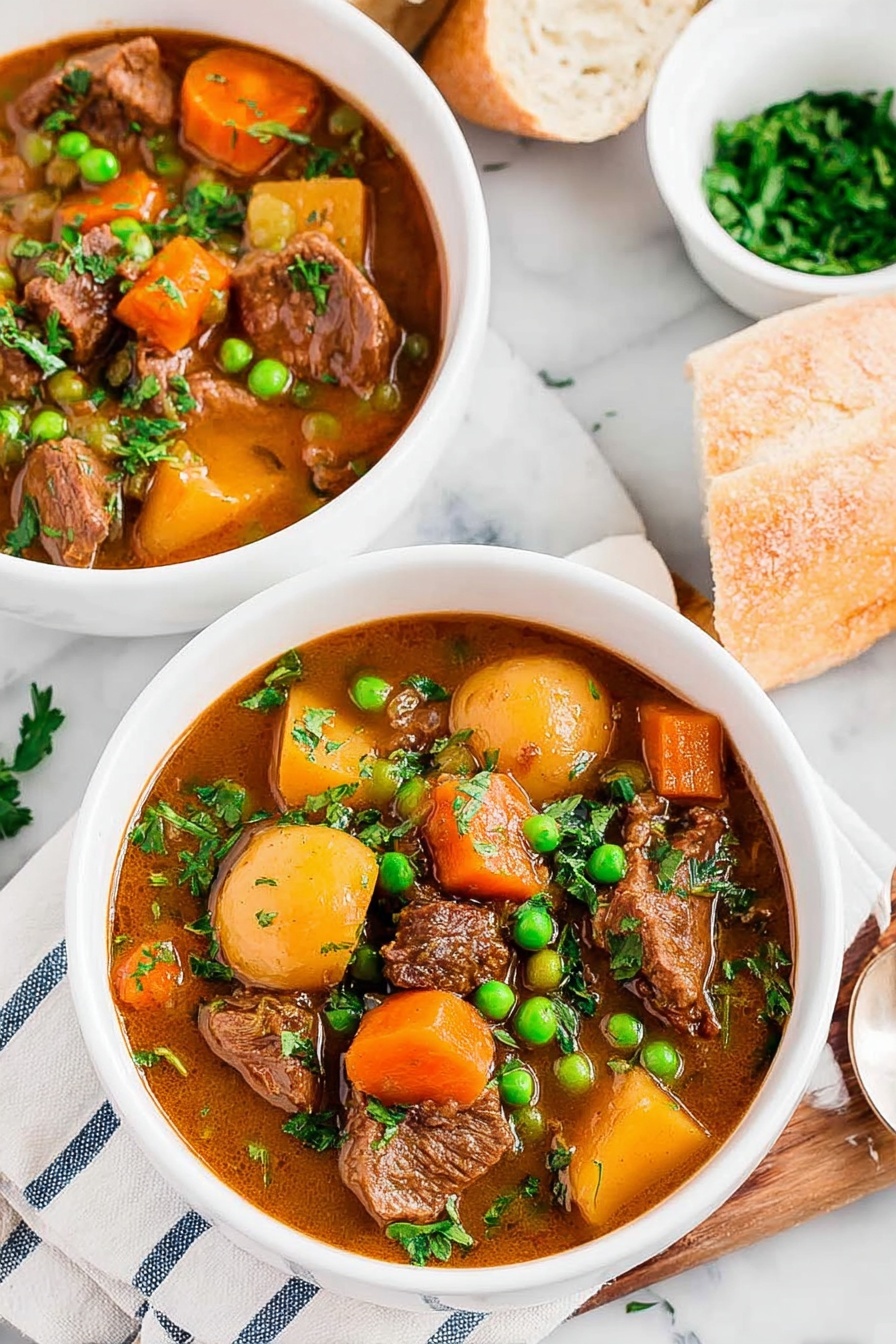 A bowl of beef stew with peas and carrots.