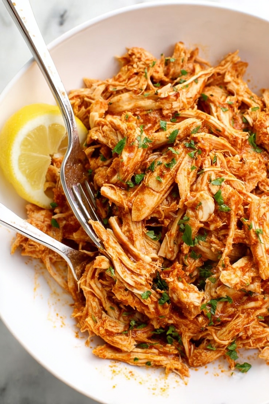 A bowl of shredded chicken with a lemon wedge on top.