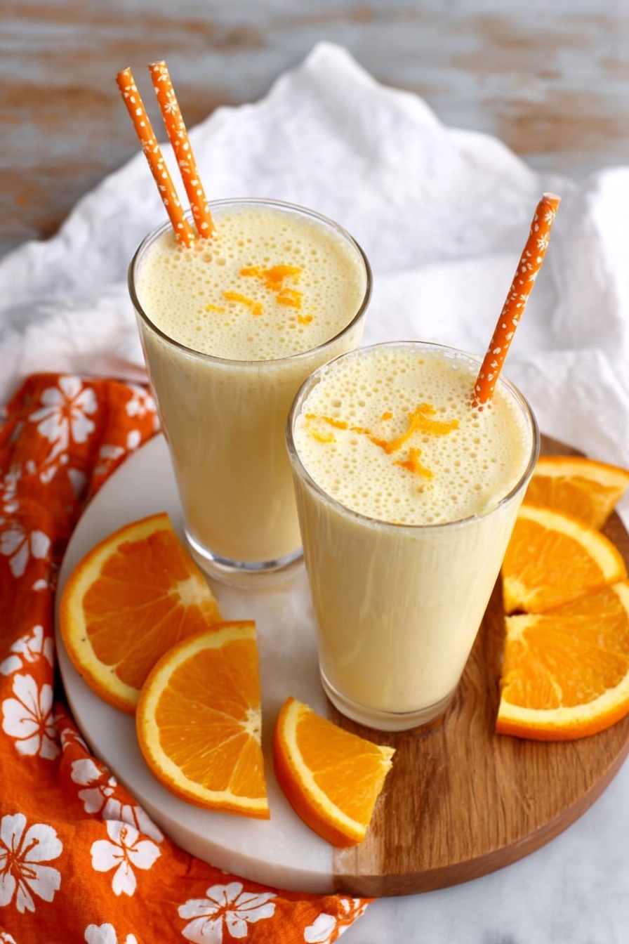 Two glasses of orange honey lassi with orange slices on a table.