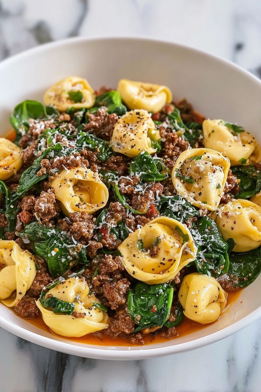 A bowl of pasta with meat and spinach.