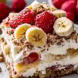 A yummy cake slice topped with bananas and sliced strawberries.