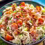 A bowl of chicken salad with tomatoes.