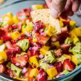 A hand grabs a piece of chips from a bowl of fruit.