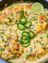 A skillet of jalapeno chicken with lime wedges on top.