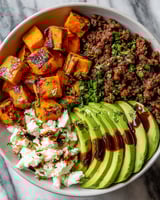 A bowl of food with a variety of ingredients including avocado, ground beef, and honey.