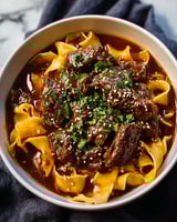 A bowl of beef noodles with a green garnish.