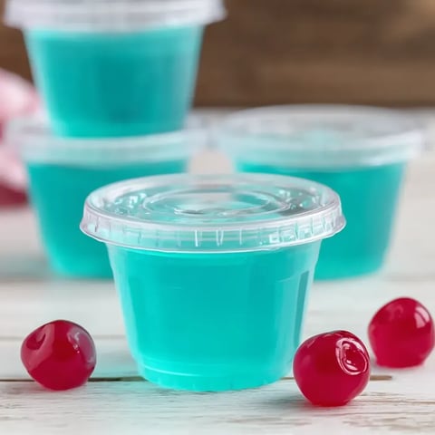 A cup of blue liquid with cherries on the side.