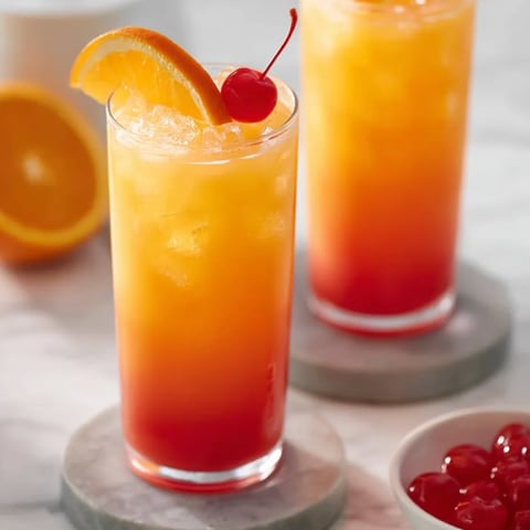 Two orange juice drinks with cherries nearby.