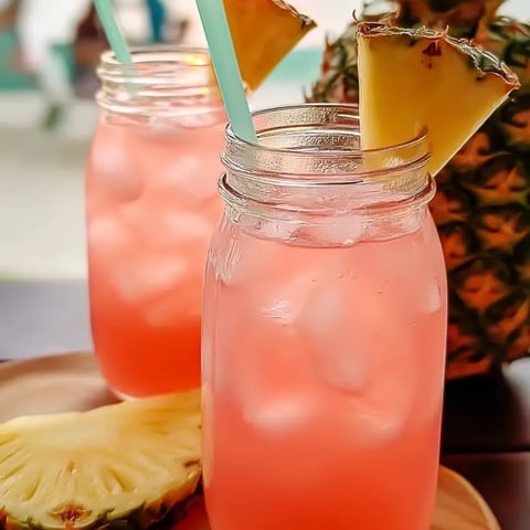 Two glasses filled with a pink fizzy drink, each topped with a pineapple wedge.