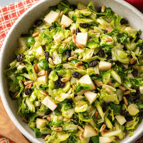 A bowl of salad with apples, nuts and greens.