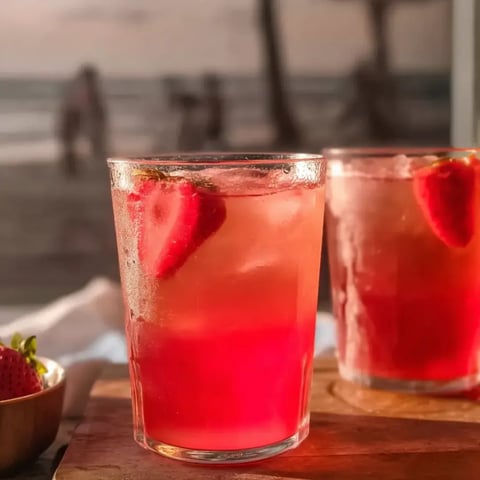 Two glasses of pink drink with strawberries in them.