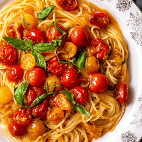 A bowl of thin spaghetti topped with tomatoes and basil.