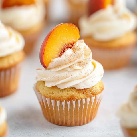 Cupcake topped with a peach slice and fluffy cream.