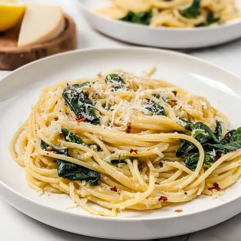 Spaghetti topped with spinach and cheese on a plate.
