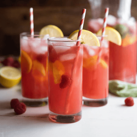 Three glasses filled with bright pink lemonade and striped straws.