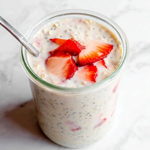 A glass filled with creamy yogurt and strawberry pieces.