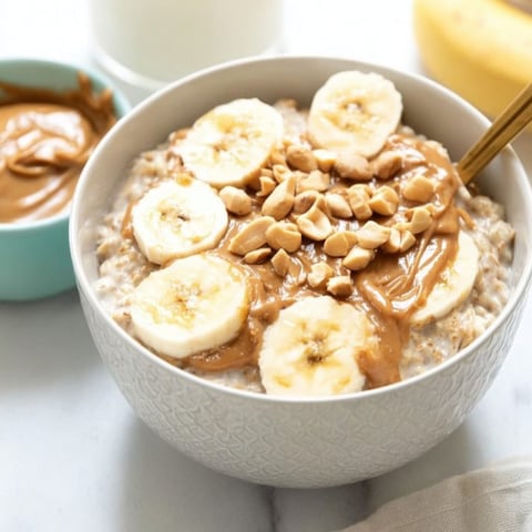 Oats topped with sliced banana and a swirl of peanut butter in a round bowl.