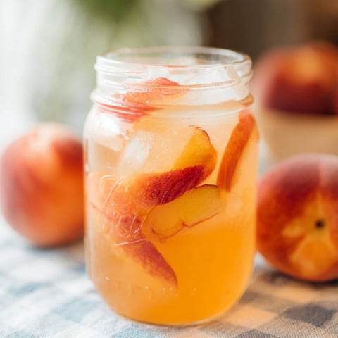 A glass of peach juice with a peach in it.