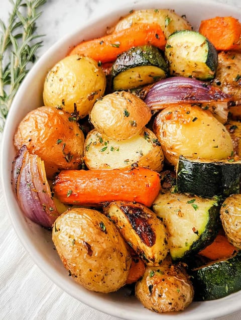 A bowl of roasted vegetables including potatoes, carrots, and zucchini.