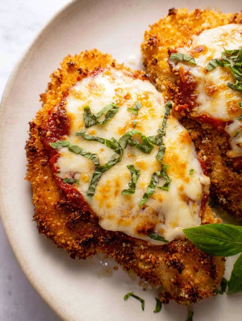 A piece of chicken with cheese and herbs on it.