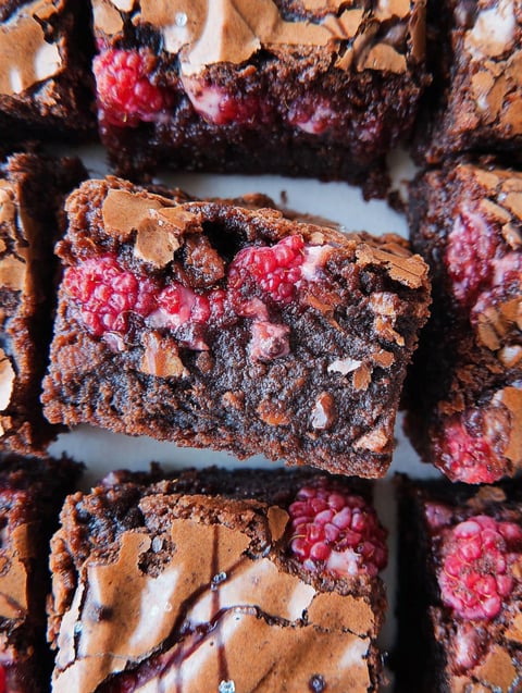 A close up of a chocolate brownie with raspberries on top.