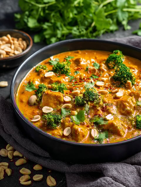 A bowl of peanut butter curry with broccoli and peanuts.