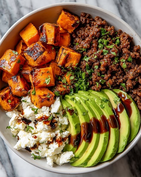 A bowl of food with a variety of ingredients including avocado, ground beef, and honey.