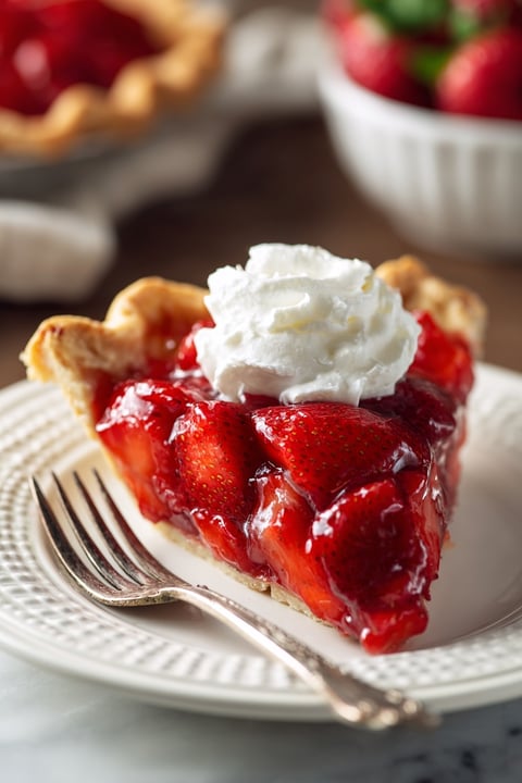 A slice of strawberry pie with whipped cream on top.