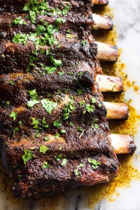A close up of BBQ ribs with herbs on top.