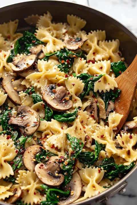 A bowl of pasta with mushrooms and spinach.