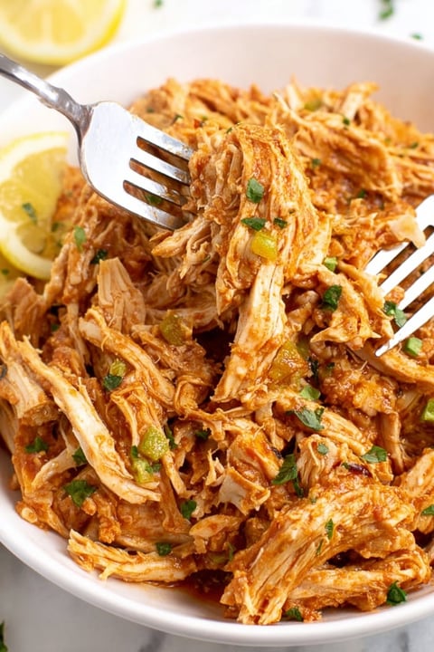A fork is stuck in a plate of shredded chicken.
