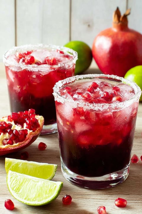 Two glasses of pomegranate margarita with limes on the side.