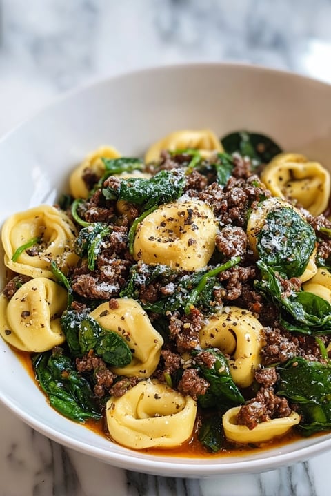 A bowl of pasta with meat and spinach.